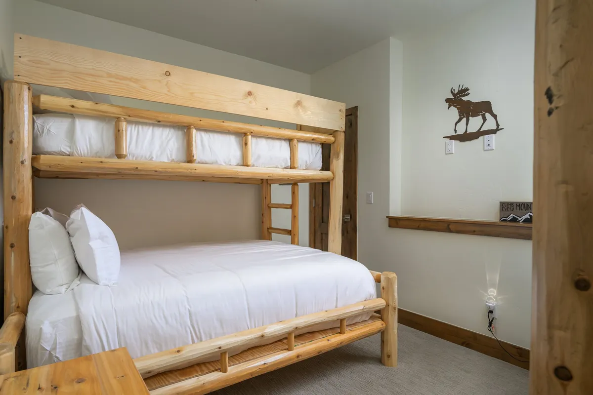 A charming bunk room with a sturdy wooden bunk bed, warm wood accents, and whimsical moose wall art. The room feels playful yet refined and offers a welcoming space for both kids and adults.