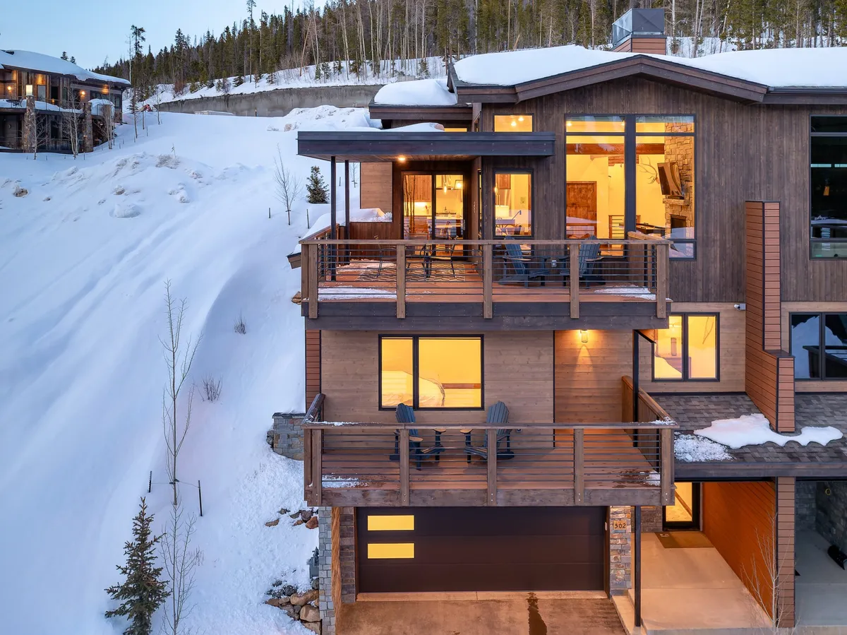 An exterior shot of the villa's balcony with chairs, large windows, and a snow-covered landscape, including a visible garage door. The scene feels welcoming and serene, showing the ideal spot to gather after a day of activities, with easy access to gear storage and the resort shuttle.
