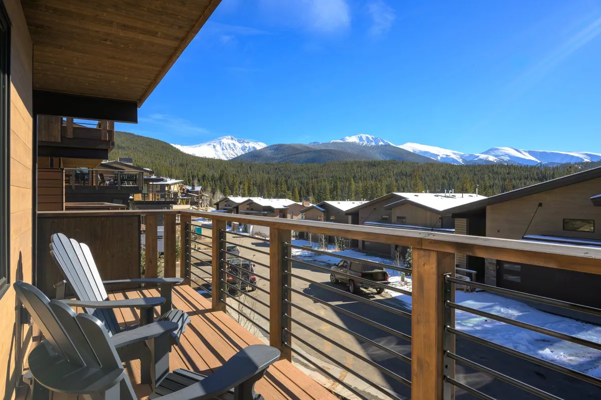 This exterior image showcases a balcony with comfortable seating overlooking breathtaking mountain views. The surrounding neighborhood is visible, emphasizing both privacy and scenic context. The relaxed setup invites guests to imagine unwinding outdoors with family and friends while soaking in the serene landscape.