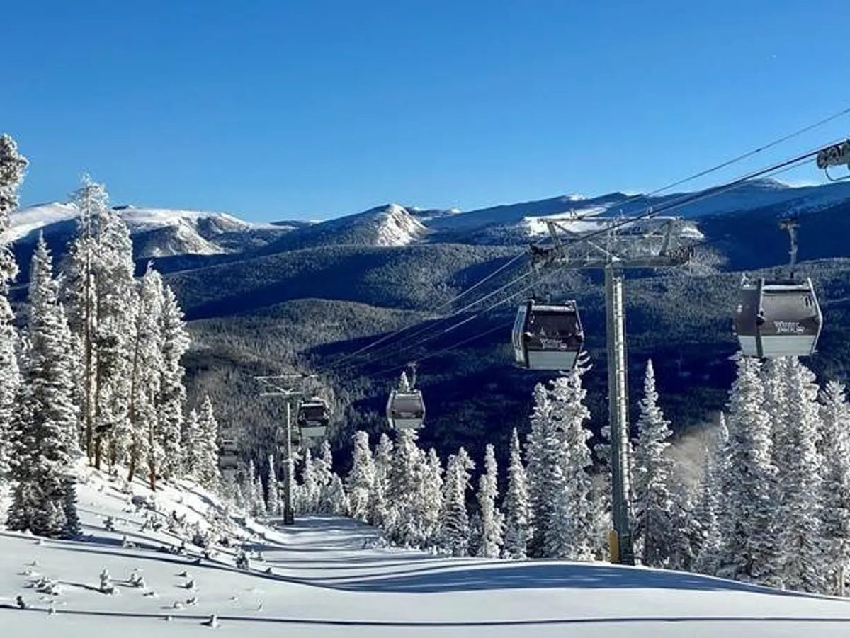 A stunning winter scene featuring ski lift chairs ascending over snow-covered slopes, with a dramatic mountain range and frosted pine trees in the background. The lively ski area is bathed in bright light, evoking the excitement of winter sports.