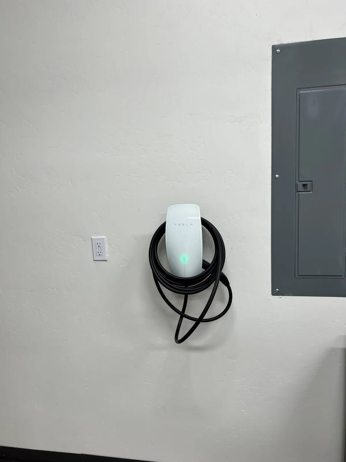 Inside a modern garage, a Tesla charging station and electrical panel are visible, reinforcing the home's advanced amenities and support for electric vehicles.