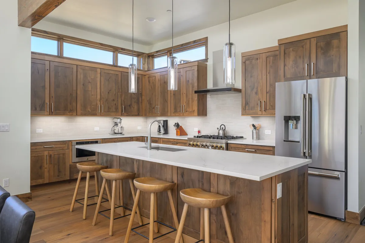 A beautifully appointed kitchen featuring a central granite island, warm wood cabinetry, stylish pendant lighting, and high-end stainless steel appliances. The layout is open, seamlessly connecting to the surrounding living space, and the counters are arranged for both group cooking and casual dining.